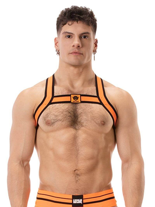 A model wearing an orange and black elastic chest harness with the BARCODE Berlin brand emblem on the front horizontal strap.