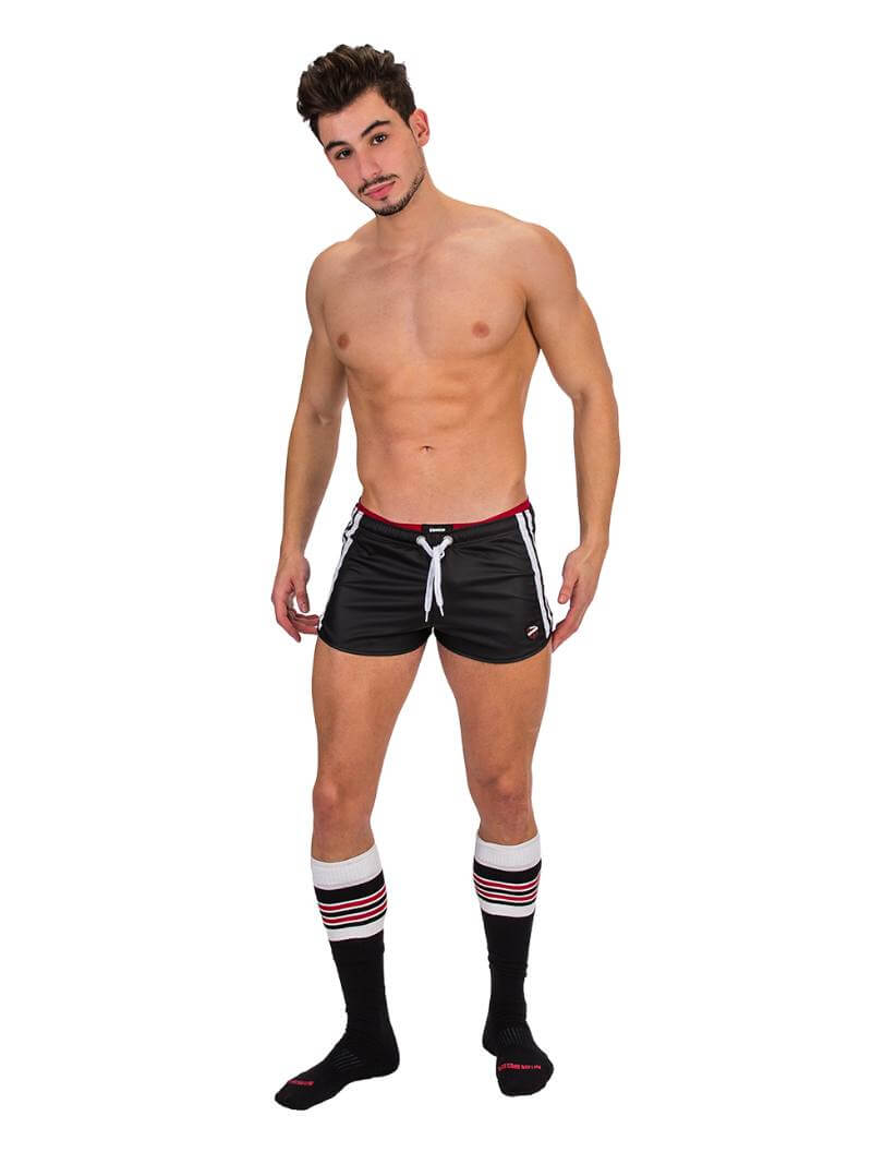 A man wearing red fishnet long-sleeve top and black mini shorts with sporty stripes and a drawstring.