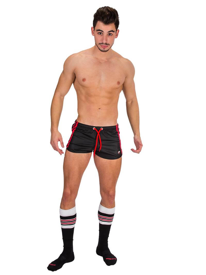 A man wearing red fishnet long-sleeve top and black mini shorts with sporty stripes and a drawstring.