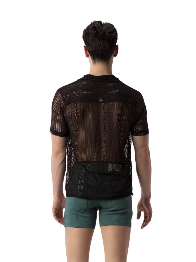 A male model wearing a black, semi-see-through lace shirt with short sleeves and a collared neck.