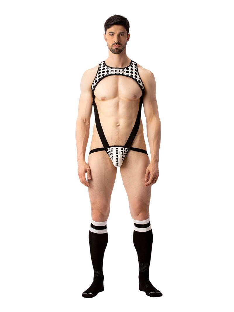 A model wearing a black and white polka dot body harness with a matching jockstrap. The harness features a chest panel, X-style back, and soft elastic straps.