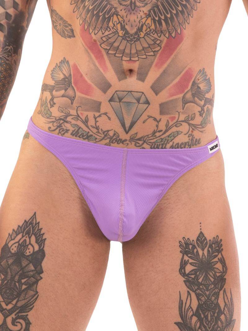 A man wearing a pink swimwear thong with a bold pattern on the waistband and high-cut legs, featuring a tattooed design on his torso.