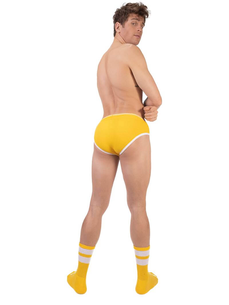 A man wearing a yellow Barcode Berlin brief with white trims and a brand logo on the waistband.