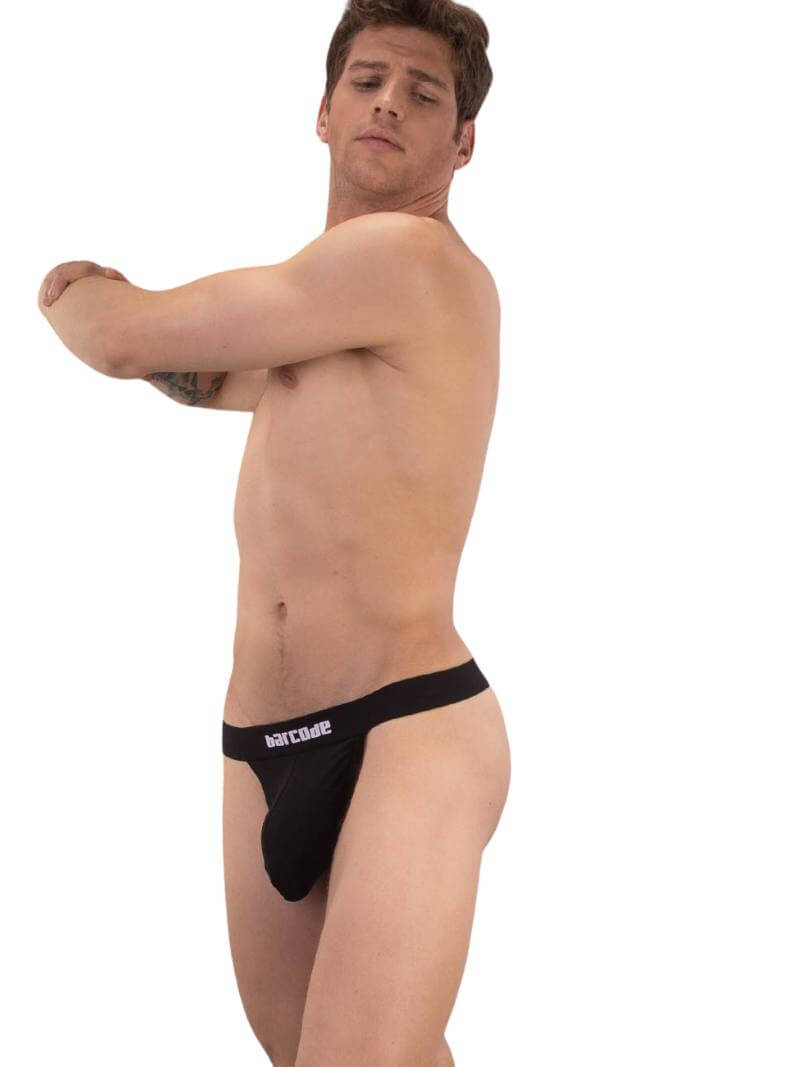 A red backless thong with Barcode branding on the waistband, featuring an elastic c-ring with 'Proud' lettering. The product is modeled by a male, showcasing the fit and design.