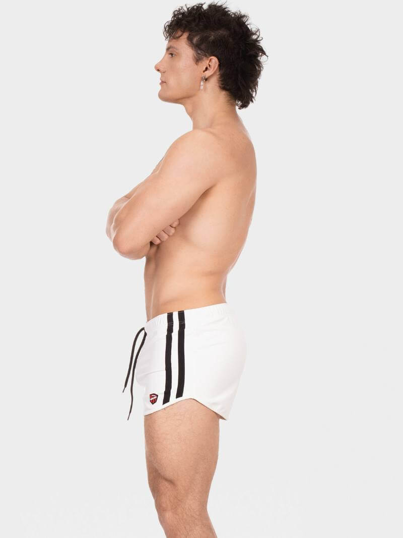 Person wearing white swim shorts with black stripes on a plain background