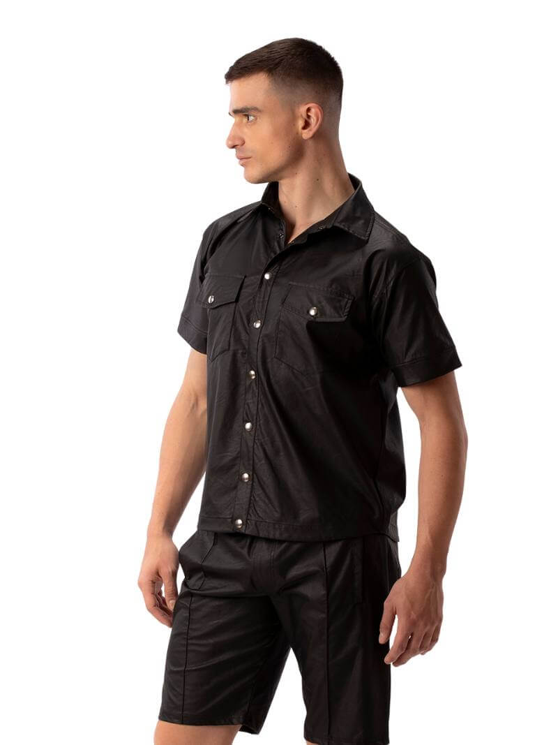 A man wearing a black faux leather shirt with metallic buttons and a collard neck, featuring short sleeves and a buttoned front.