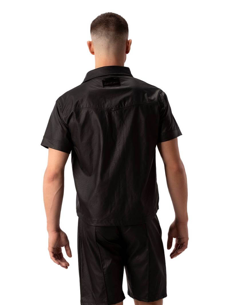 A man wearing a black faux leather shirt with metallic buttons and a collard neck, featuring short sleeves and a buttoned front.