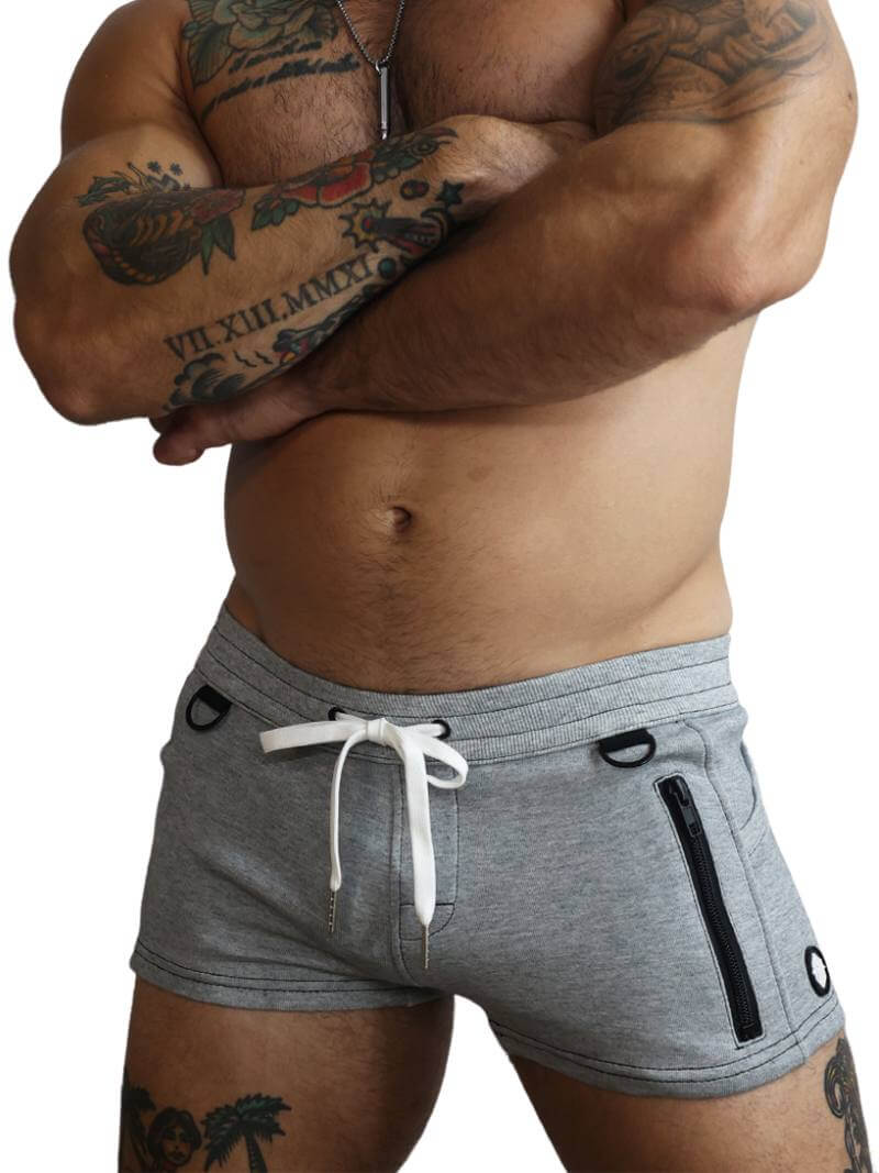 A person with tattoos wearing navy blue mini shorts with a drawstring, featuring a low-rise waist and super short legs, in a mechanical setting.