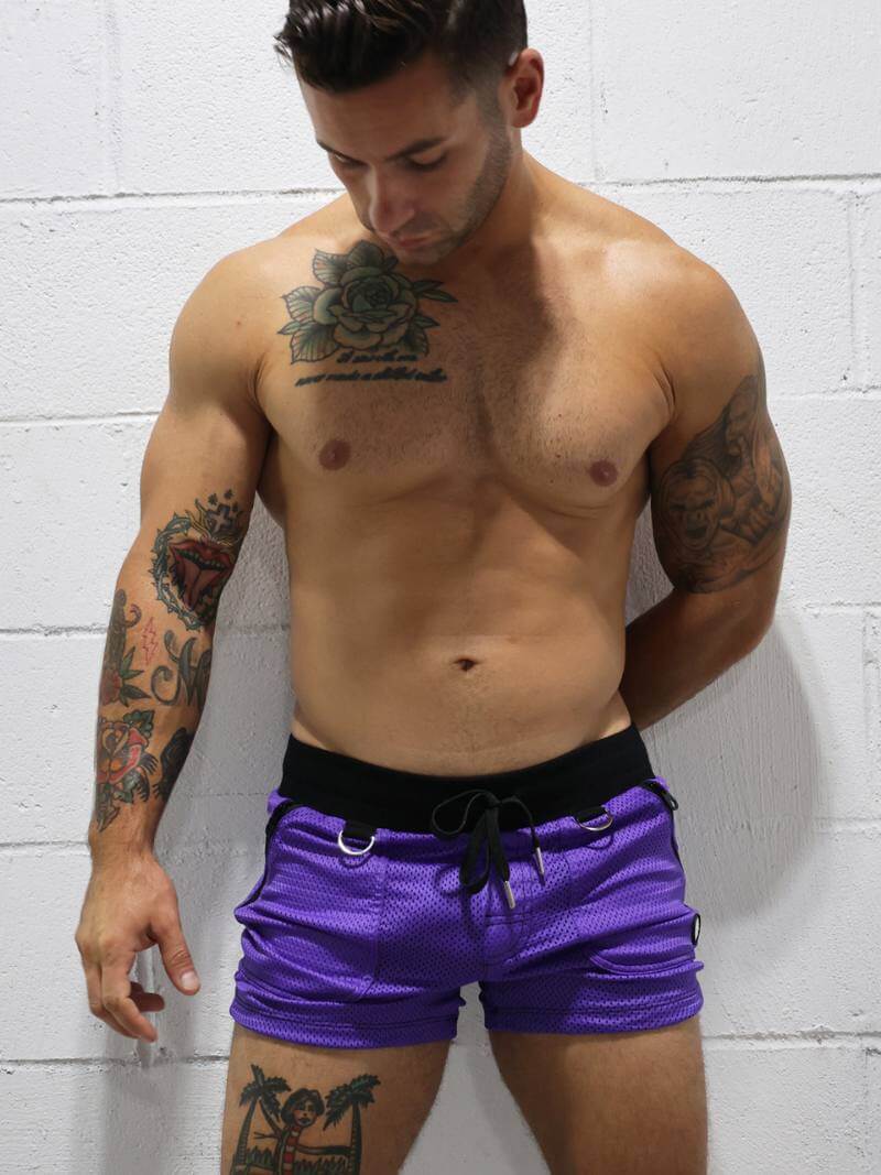Man wearing purple shorts with tattoos on a white brick wall background