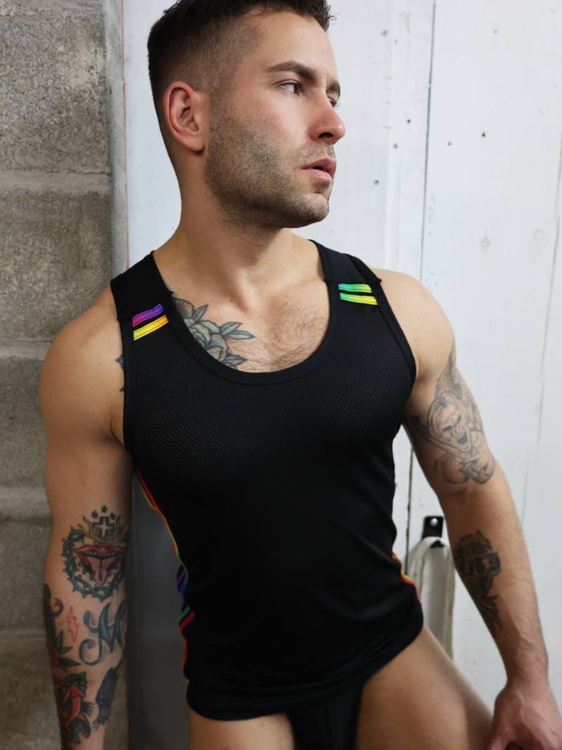 Man wearing a black tank top with colorful straps against a white wall.