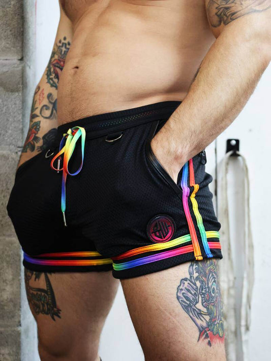 Person wearing black shorts with rainbow accents and a logo, standing against a neutral background.