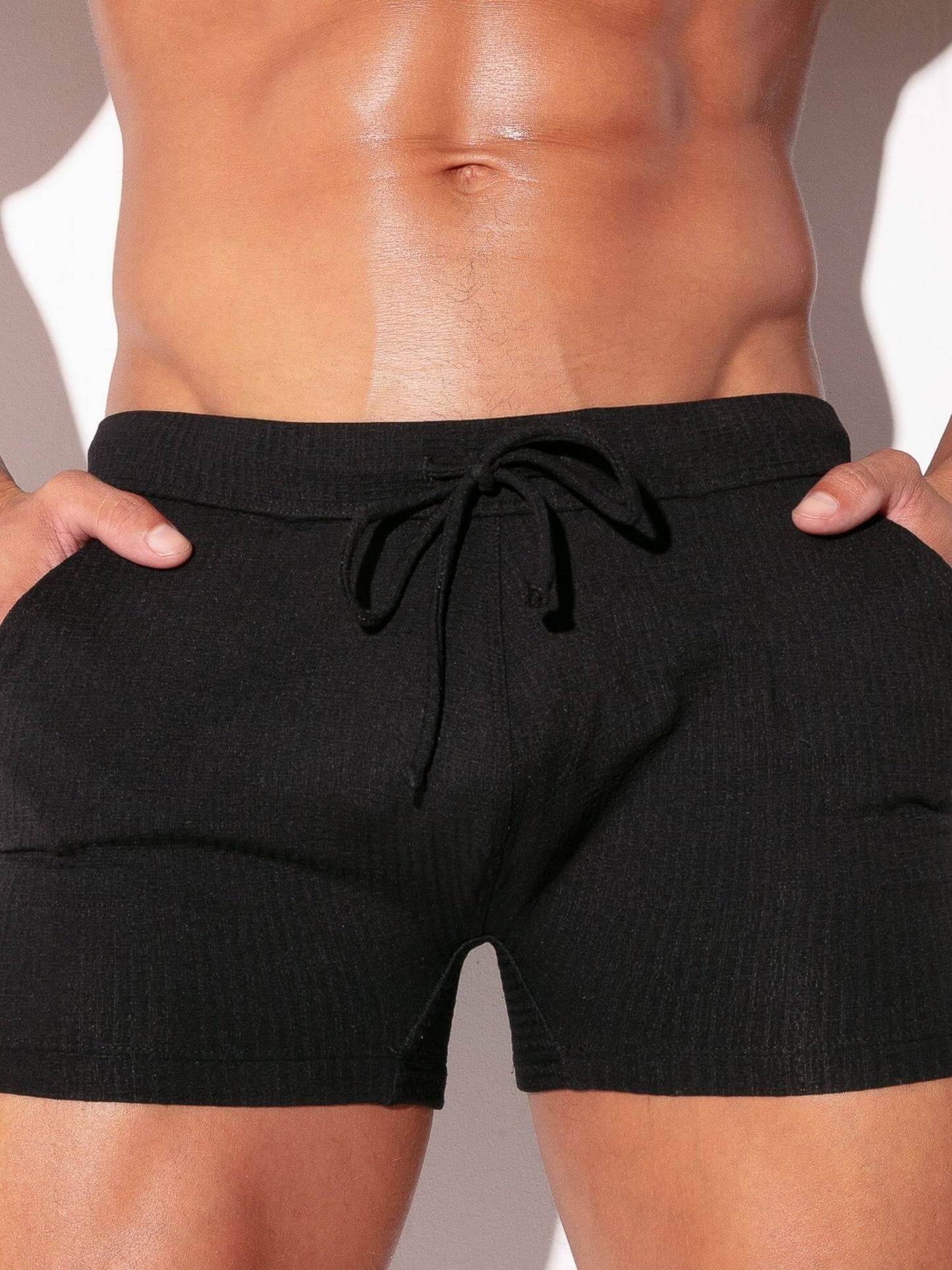 Black swim shorts worn by a person against a neutral background
