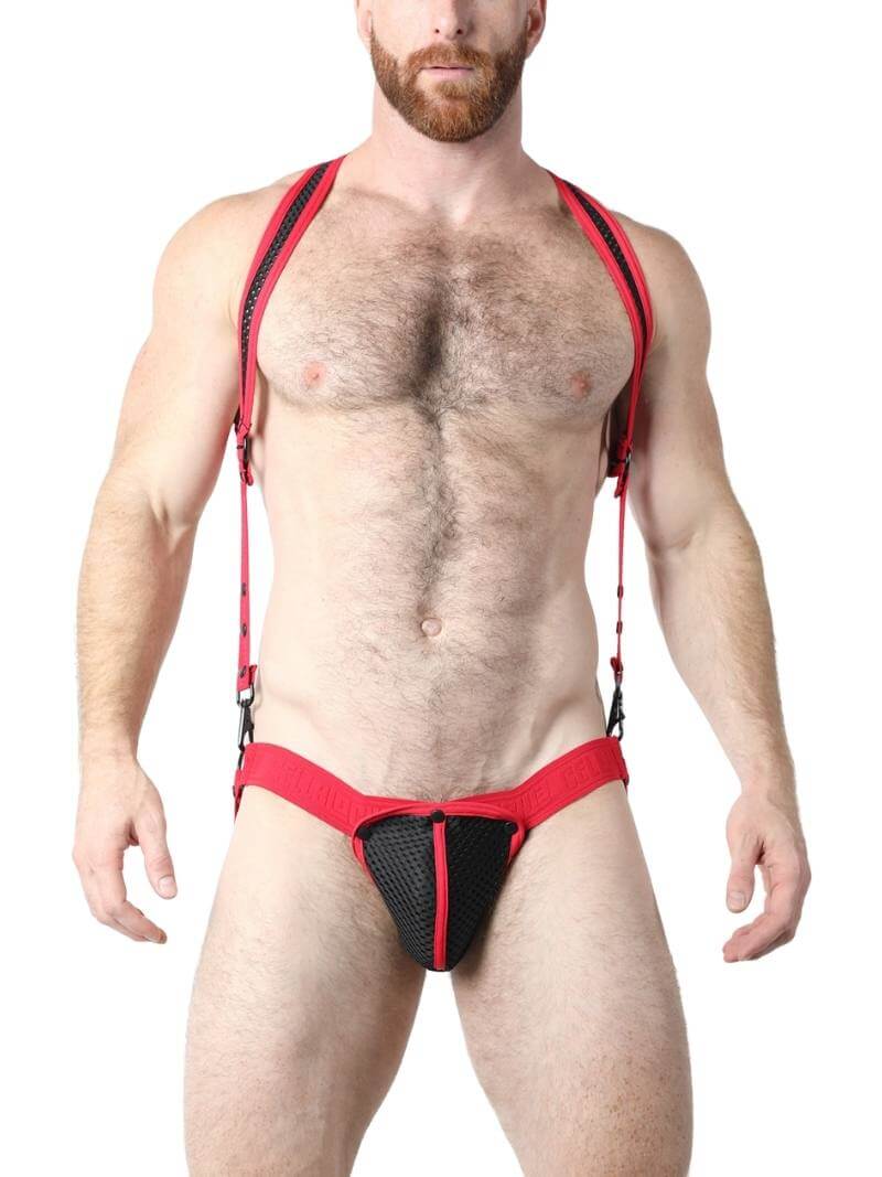 A model wearing a black mesh body harness and jockstrap set with green trim and black metallic hardware. The harness is adjustable with buckles and snaps.