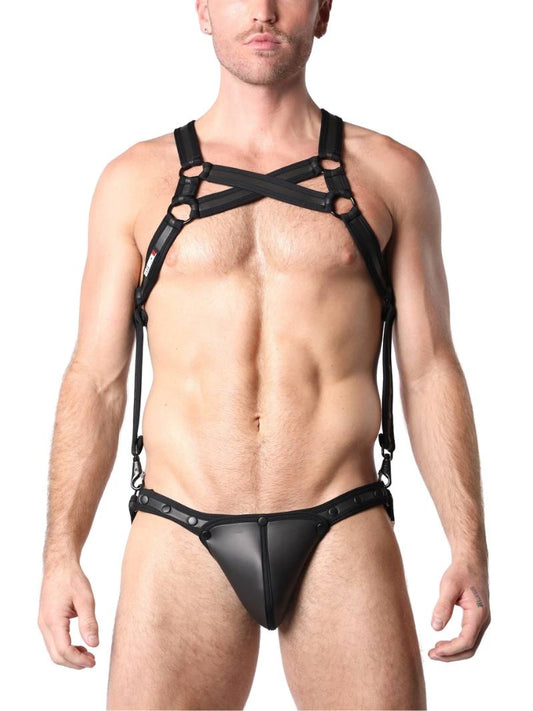 A model wearing a black neoprene body harness with double cross straps across the chest and a jockstrap. The harness has metallic rings and buckles, and the pouch is detachable.