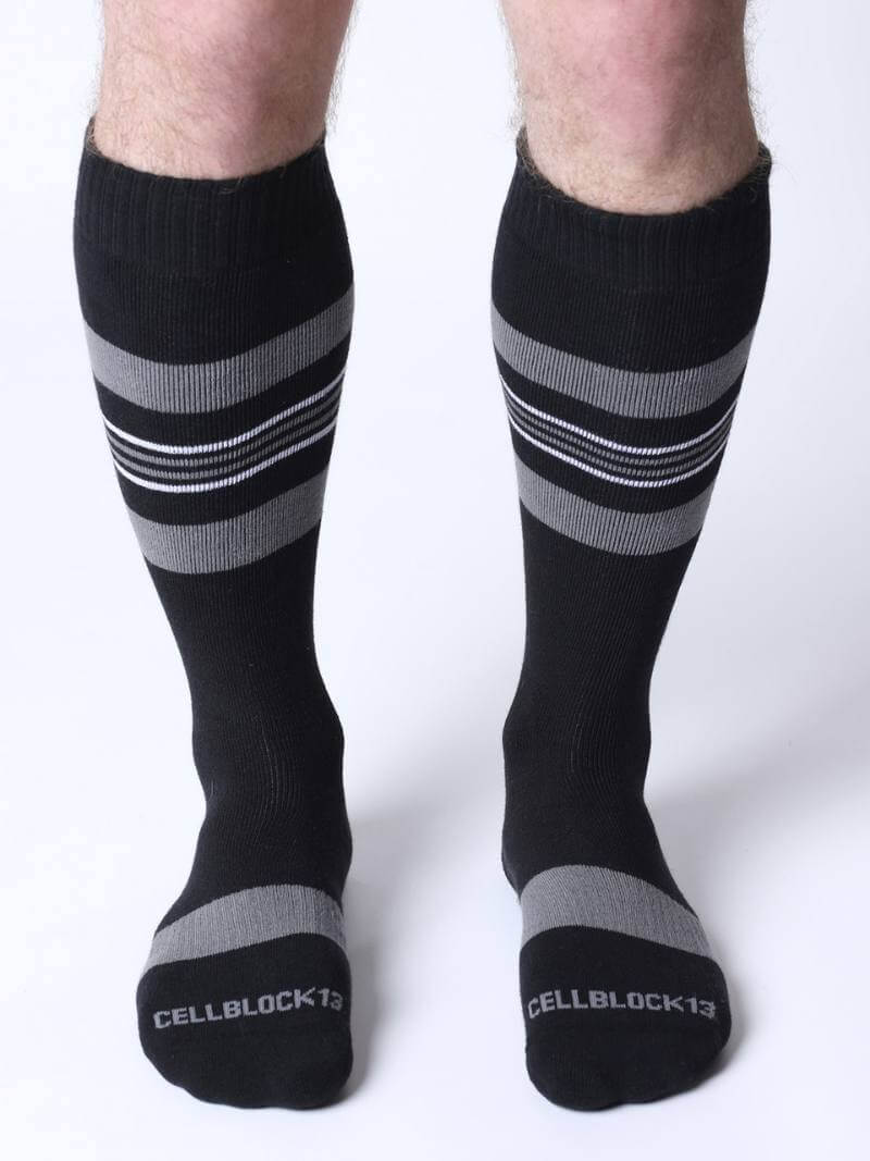 Black knee-high socks with gray stripes worn by a person on a white background