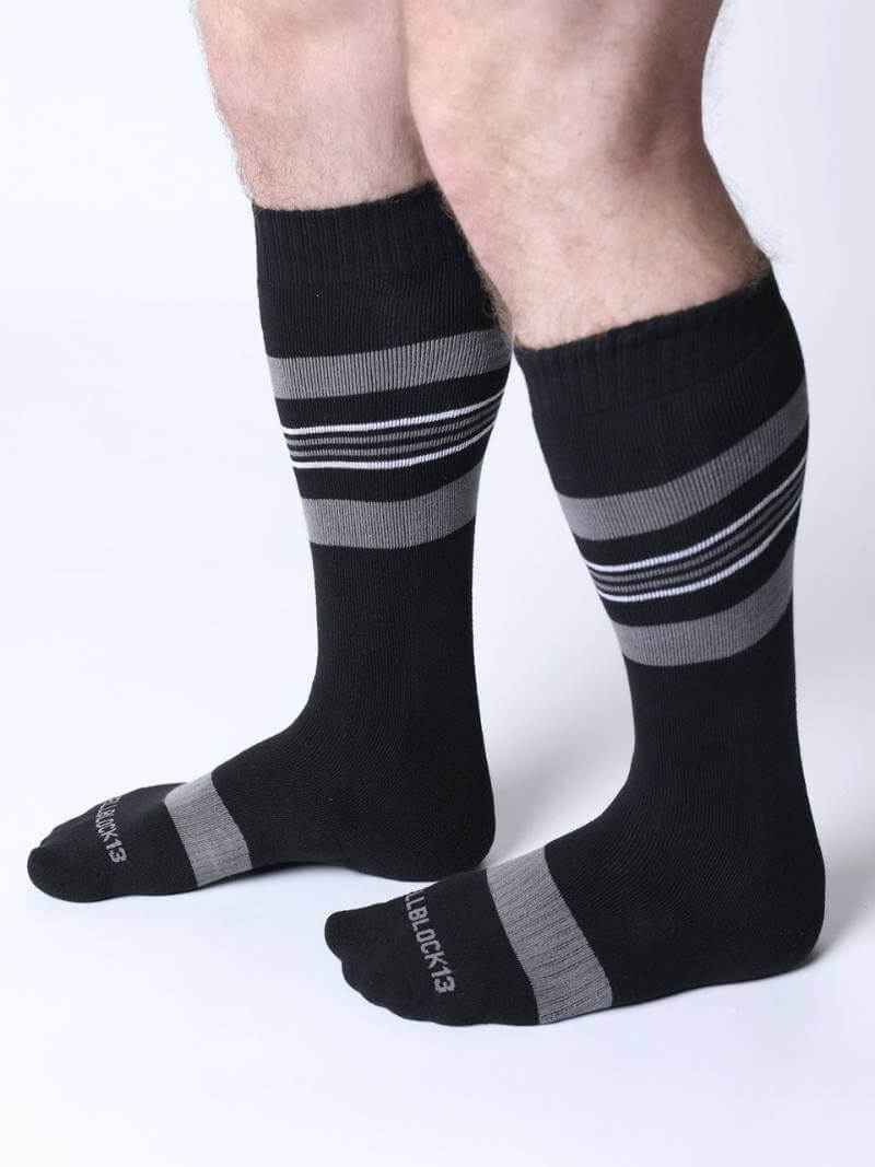 Black knee-high socks with gray stripes worn by a person on a white background