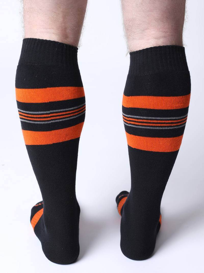 Black knee-high socks with orange stripes worn by a person on a white background