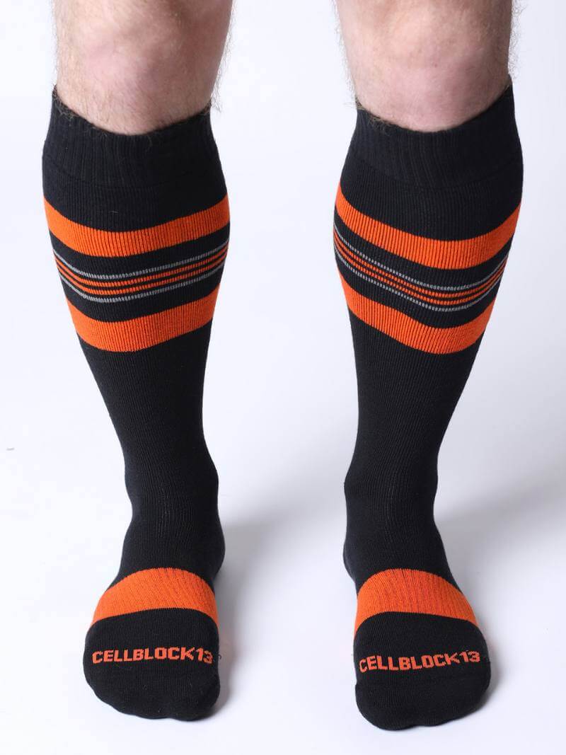 Black knee-high socks with orange stripes and 'CELLBLOCK 13' branding on a white background.
