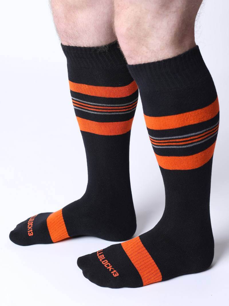 Black knee-high socks with orange stripes worn by a person on a white background