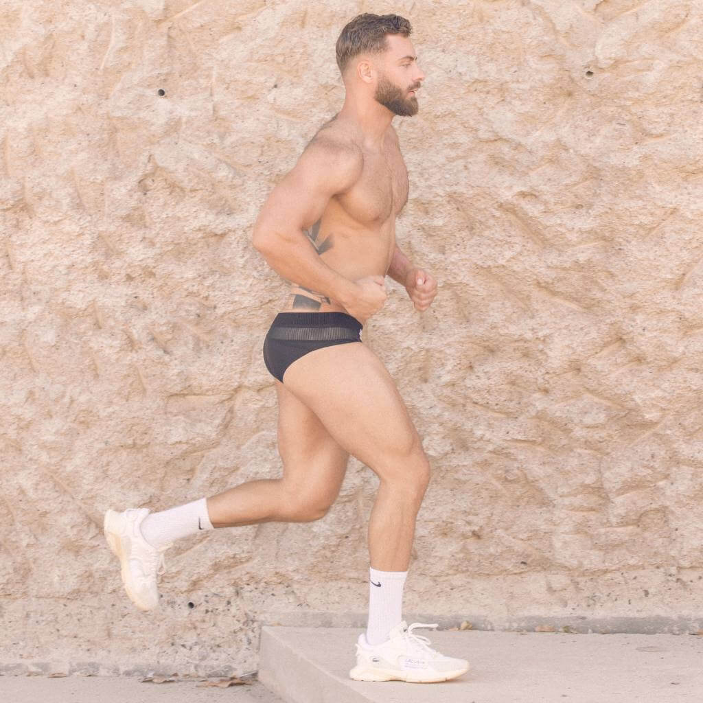 Man running outdoors against a textured wall, wering 2eros Aktiv black briefs