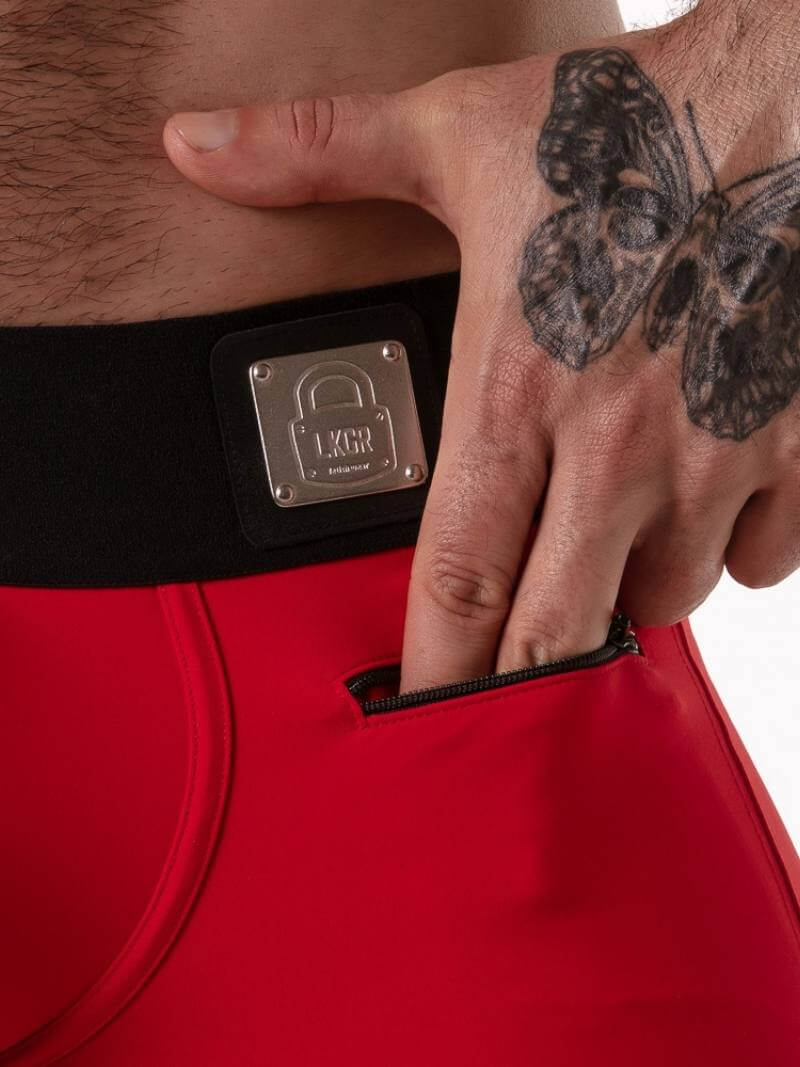 Red bag with a black strap featuring a metallic lock, held by a tattooed hand.