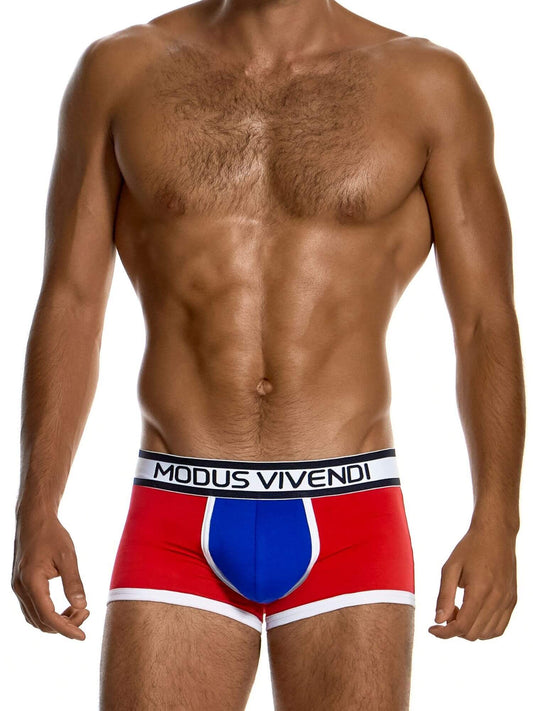 A close-up of a man's lower torso wearing Modus Vivendi boxer briefs. The underwear features a bold red base with a blue central panel and white trim, including a black and white waistband with the brand name 'MODUS VIVENDI' printed in white.