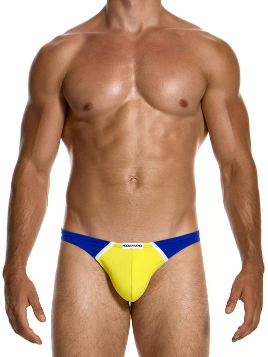 A muscular male model wearing a low-rise swim brief with a bright yellow front pouch, blue side panels, and a white center stripe with the brand name