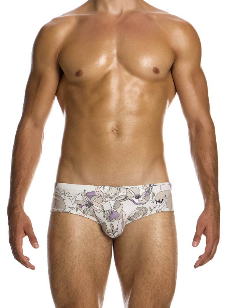 A male model wearing a Modus Vivendi Art Nouveau floral swim brief in pastel colors with a transparent brand label.