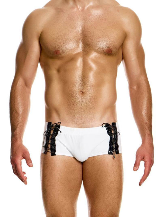 This image displays the MODUS VIVENDI Boudoir Brazil Cut Swim Trunk, featuring a smooth black fabric with shiny corset-style lace-up sides. The swim trunk is designed with a Brazil cut that includes super-short legs and a low-rise waist, offering a stylish and cheeky silhouette.