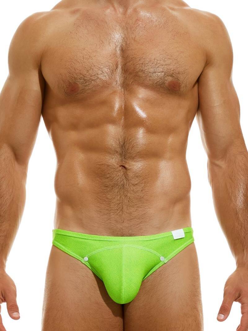 A man wearing a neon green 'MODUS VIVENDI Jeans Mini Swimming Brief' with decorative press studs and a silicone brand logo.