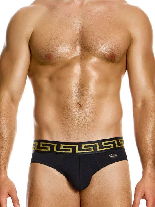 A model wearing black Modus Vivendi Meander briefs with a gold and silver Greek key print on the waistband and a brand charm logo.