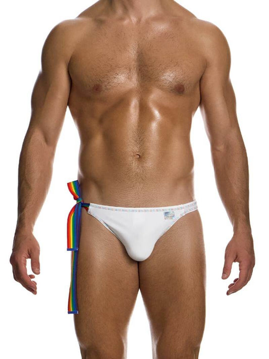 This image features the MODUS VIVENDI Pride Swimwear Thong, designed with a white body and highlighted with rainbow-colored stitching. The swimwear includes a rainbow-striped side ribbon and a shiny holographic sewn Modus Vivendi logo, adding a distinctive touch of style and pride.