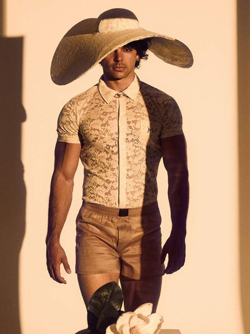 Person wearing a wide-brimmed hat, patterned shirt, and shorts against a neutral background