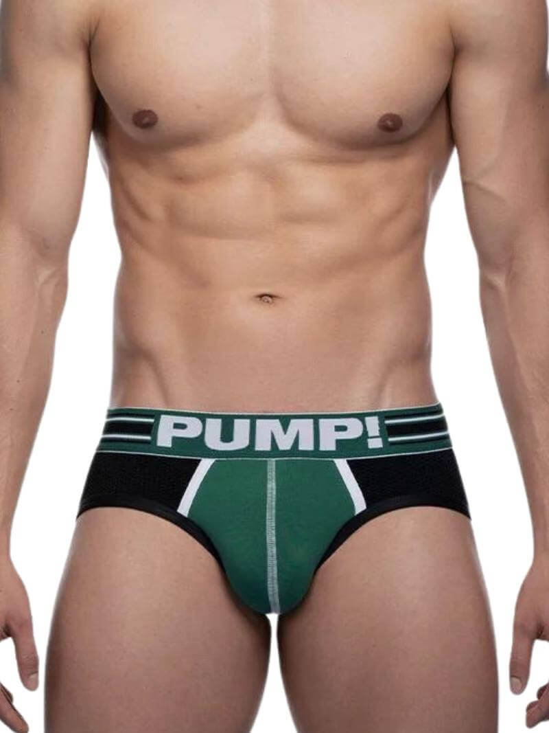 A model wearing a PUMP Underwear Boost Jockstrap with contrasting green and black panels on the body and black elastic straps. The waistband is striped and has the PUMP branding.