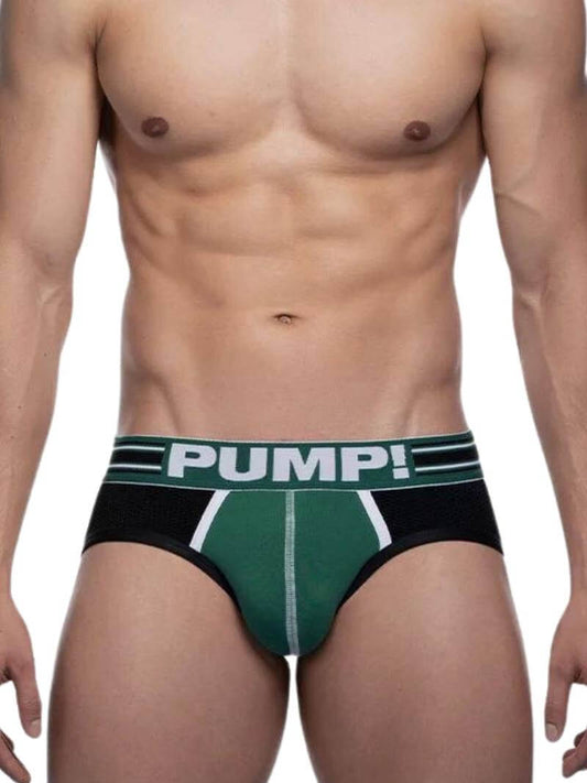 A model wearing a PUMP Underwear Boost Jockstrap with contrasting green and black panels on the body and black elastic straps. The waistband is striped and has the PUMP branding.