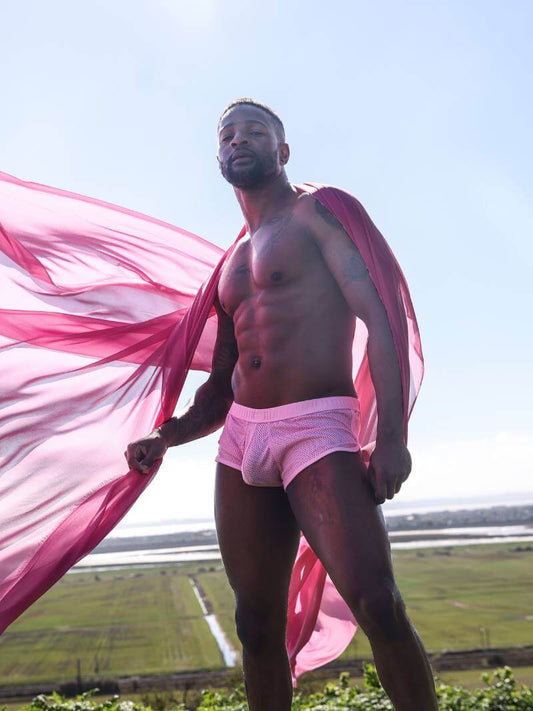 Man wearing pink underwear holding a pink fabric in an outdoor setting