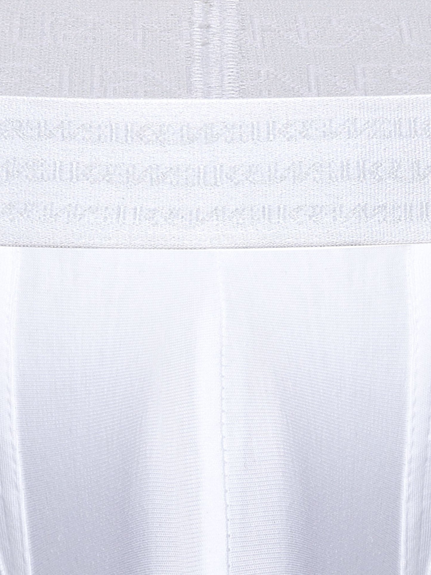 Close-up of a white underwear or garment waistband with a repeating tonal SUKREW logo pattern, shown against matching white fabric.