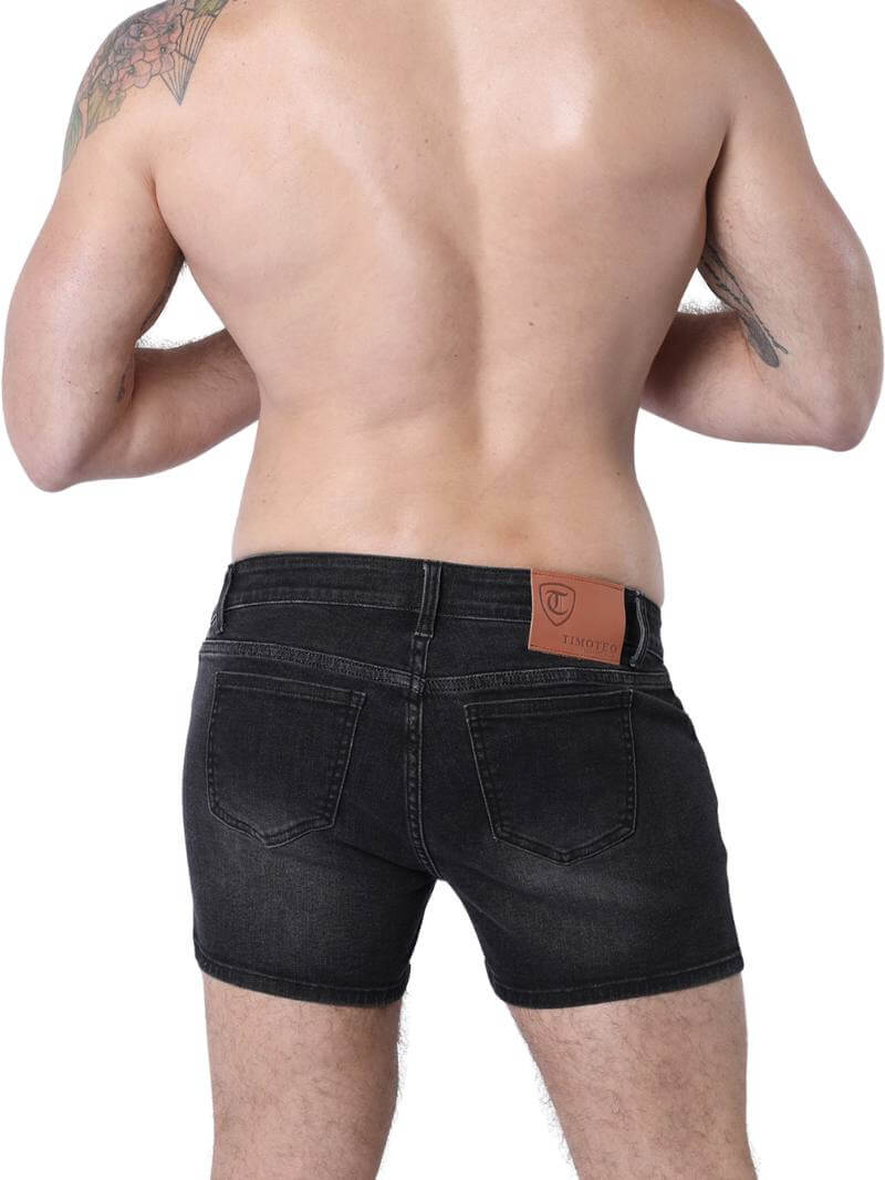 A pair of denim booty shorts with a low-rise waist and a 4-inch inseam, featuring a zipper fly, button fastening, belt loops, and four pockets. The shorts are blue with contrast stitching, and there is a leather branded patch on the back.