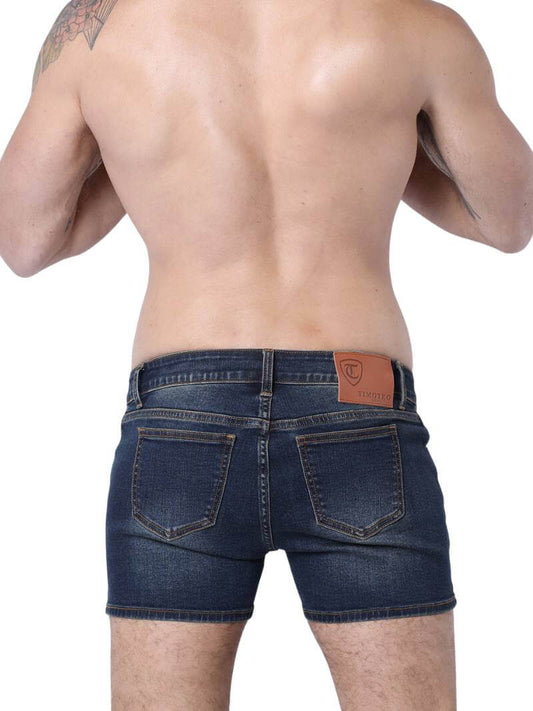 A pair of denim booty shorts with a low-rise waist and a 4-inch inseam, featuring a zipper fly, button fastening, belt loops, and four pockets. The shorts are blue with contrast stitching, and there is a leather branded patch on the back.