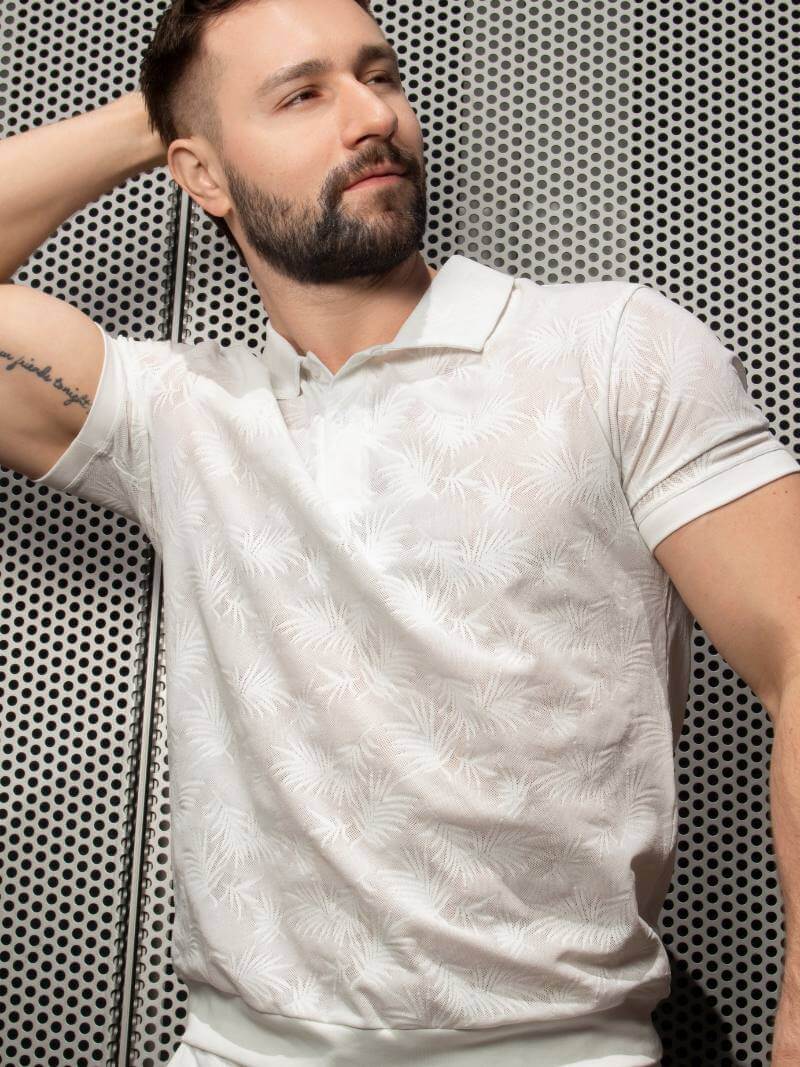 Man wearing a white patterned shirt against a perforated metal background