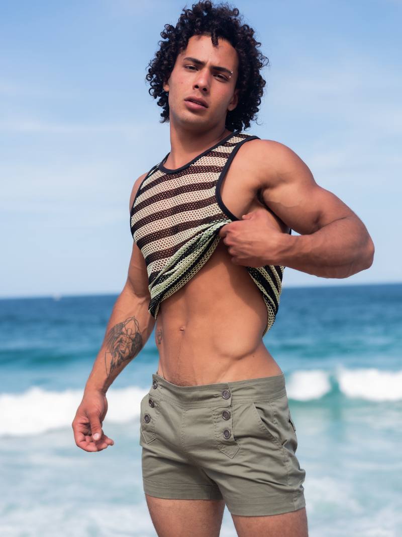 Man on a beach wearing a striped tank top and shorts with ocean in the background