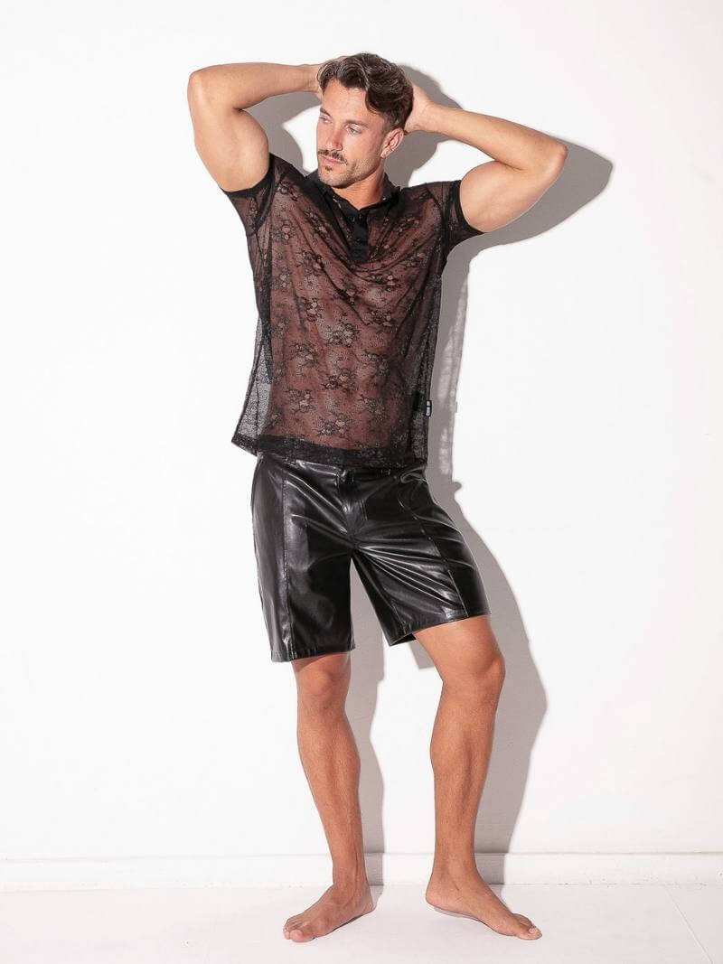 Man wearing a sheer black top and shiny black shorts on a white background