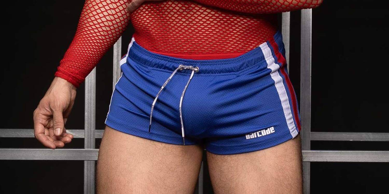 Person wearing red top and blue shorts with white stripes, standing against a dark background.