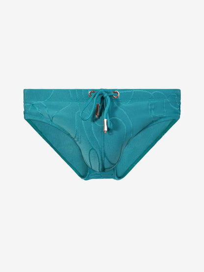 A pair of bikini bottoms featuring a subtle tonal abstract pattern, a front drawstring tie, and a small gold-tone  detail at the center front, displayed against a solid light gray background.