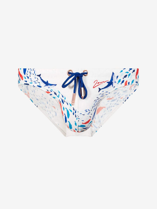 White bikini bottoms featuring a blue and red abstract print with shark motifs, a blue drawstring with gold-toned metal rings, and a red script logo on the right side.
