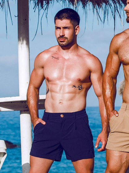 Two men standing by a body of water, one wearing navy shorts and the other in beige shorts.