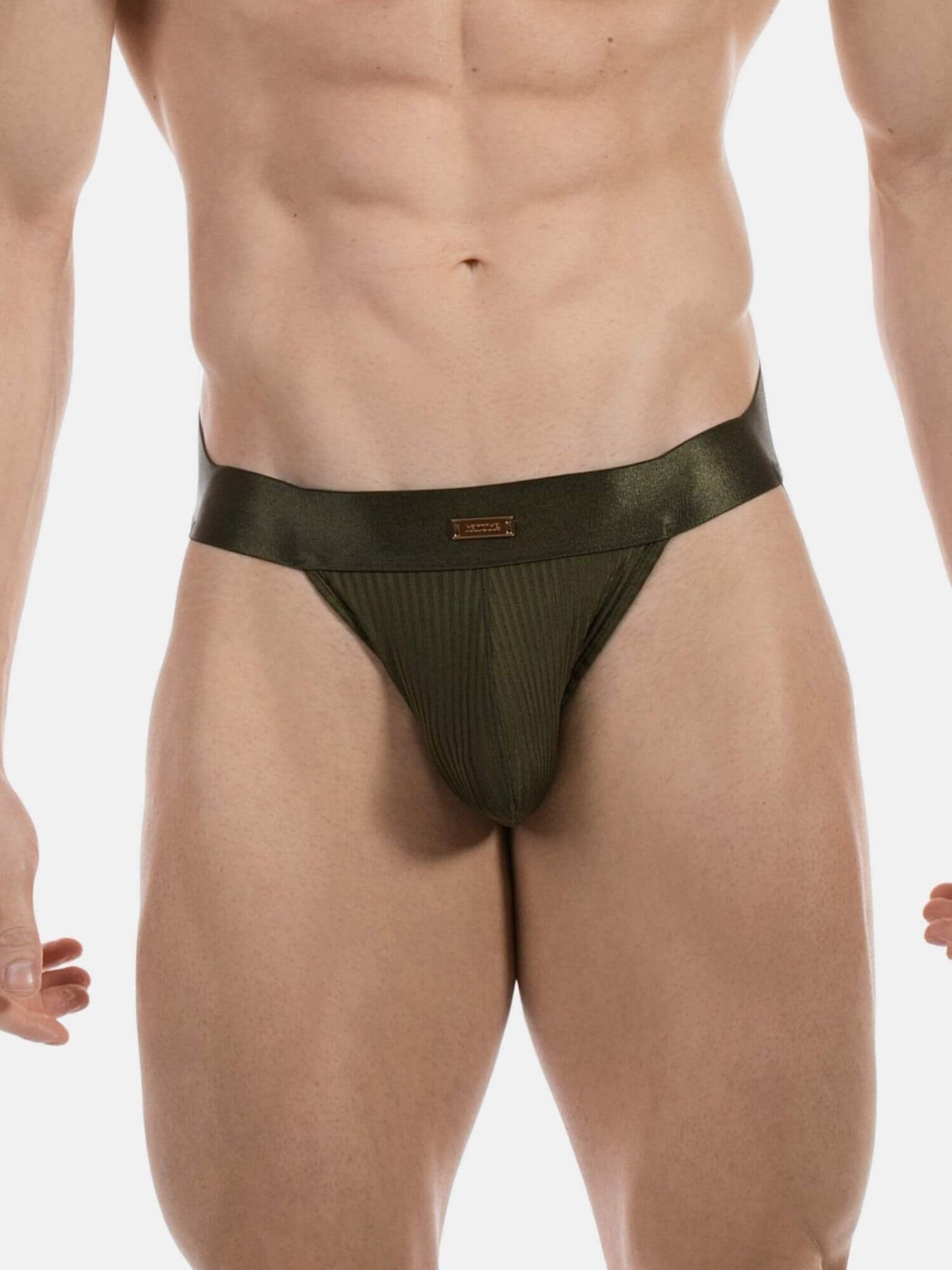 A close-up of a male model's lower torso wearing a dark olive green ribbed jockstrap with a wide matching waistband and a small gold logo plaque.