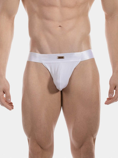 A close-up of a male model's lower torso wearing a white ribbed jockstrap with a wide elastic waistband and a small gold rectangular logo plaque at the center front, against a light gray studio background.