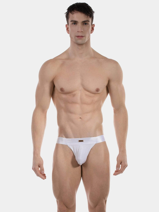 A muscular male model wearing a pair of white low-rise jockstraps standing against a solid light gray background.