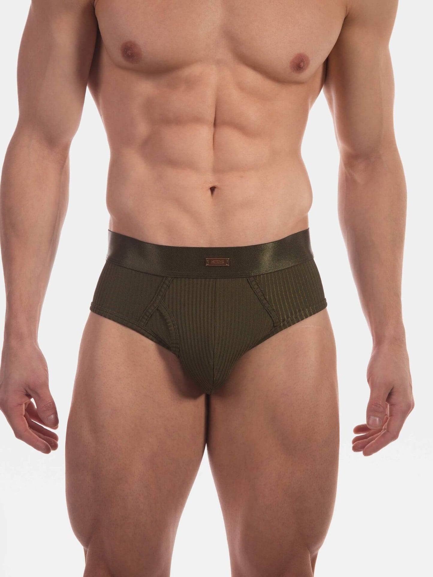A close-up of a male model wearing low-rise, ribbed olive green briefs against a plain white studio background.